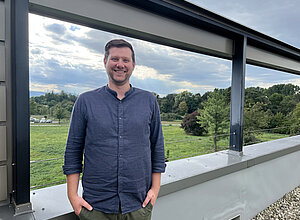Sven Nagelsdiek stands in a blue shirt on a roof terrace with a meadow in the background.