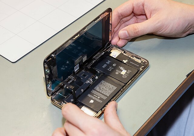 Zwei Hände halten ein geöffnetes Smartphone, das auf einer grauen Arbeitsplatte liegt.