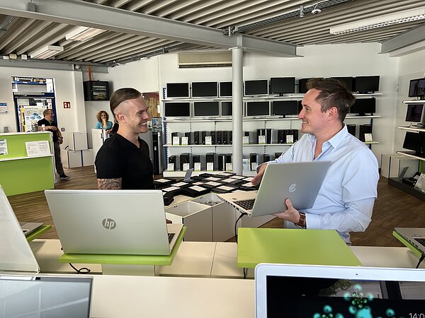 Zwei Männer stehen in einem Geschäft mit Hardware und sprechen über einen Laptop.
