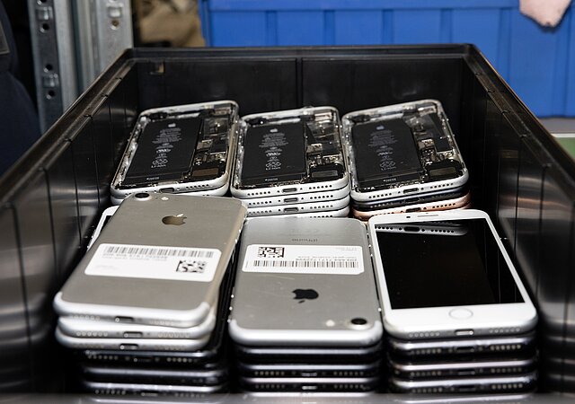 In einer schwarzen Box liegen iPhones in zwei Stapeln. Die Smartphones in der hinteren Reihe sind offen und das Innenleben sichtbar.